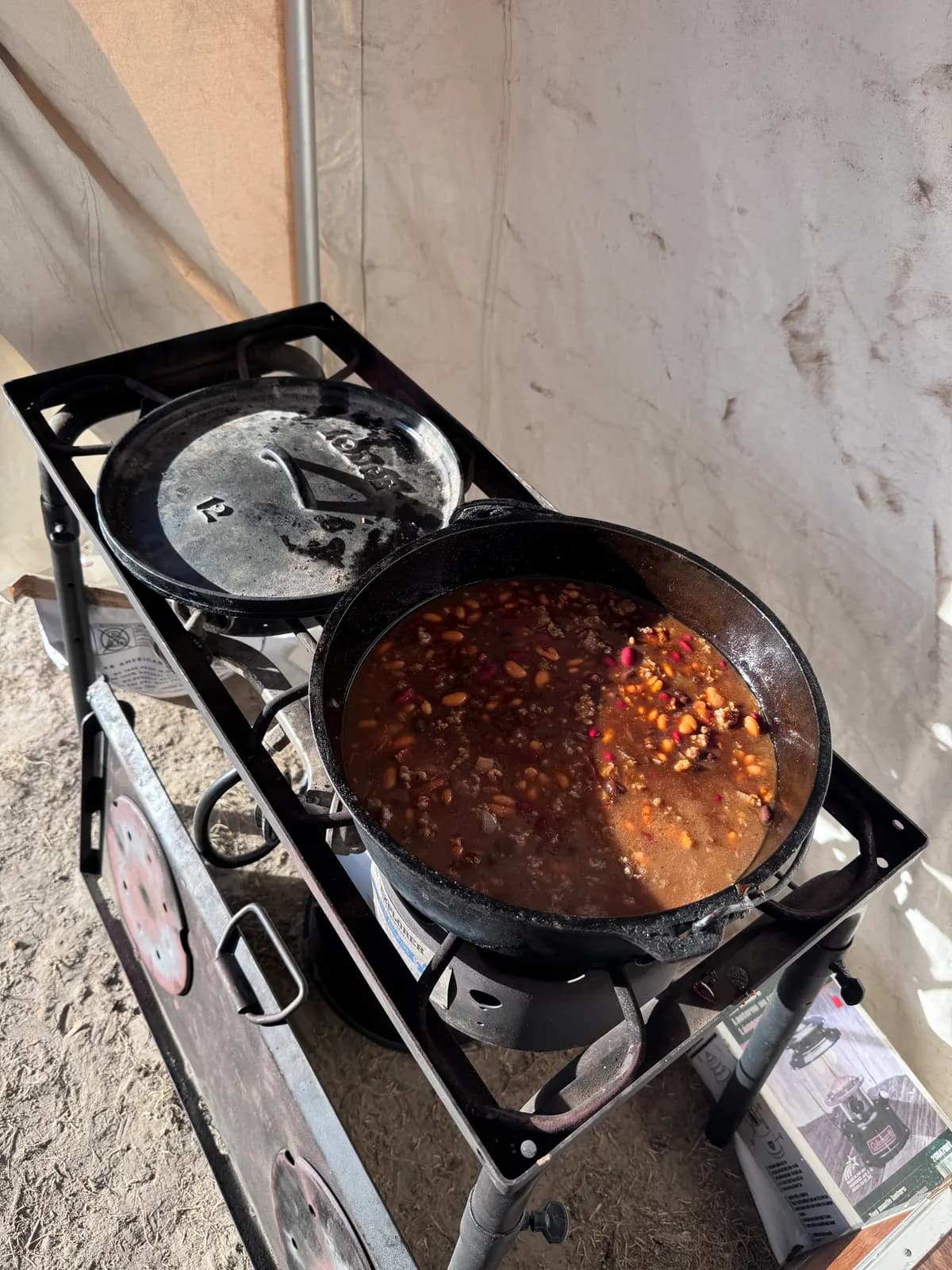A cast iron Dutch oven of chili on a Camp Chef two-burner stove.