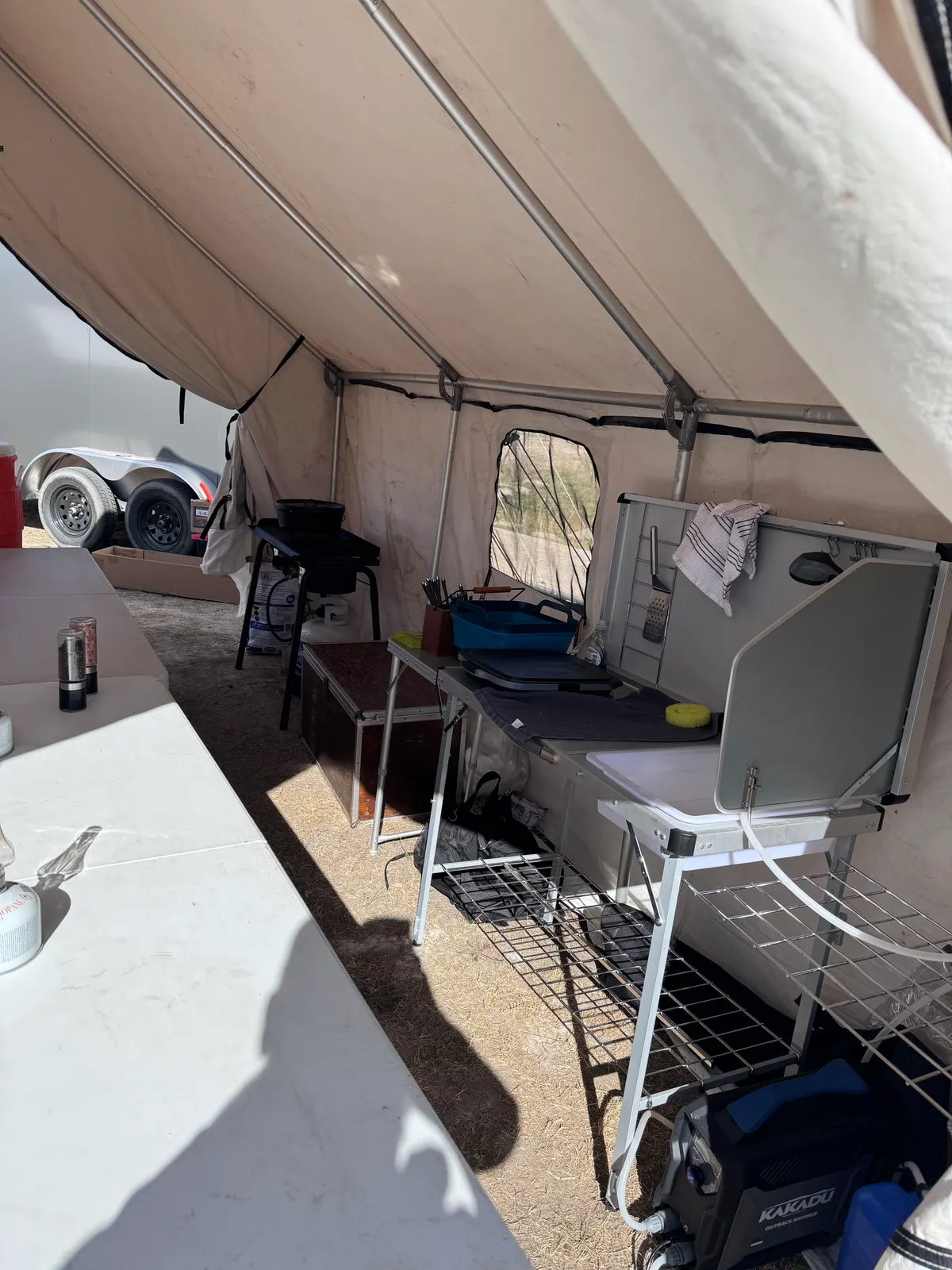 Inside a canvas cook tent: a folding camp kitchen with a sink and shelves, a cutting board, and a stove along the far wall.
